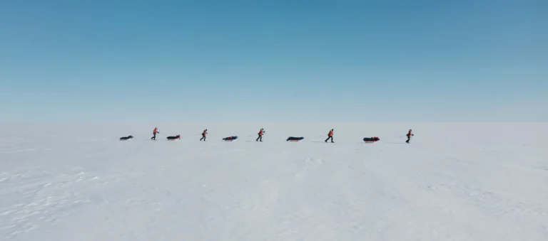 A group of scientists crossing ice on skis with pucks behind them